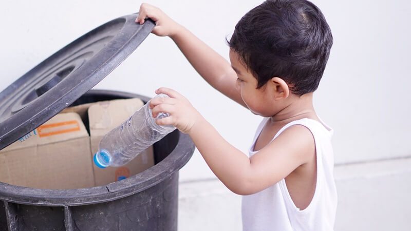 budak lelaki buang sampah ke dalam tong sampah sebagai amalan kebersihan diri